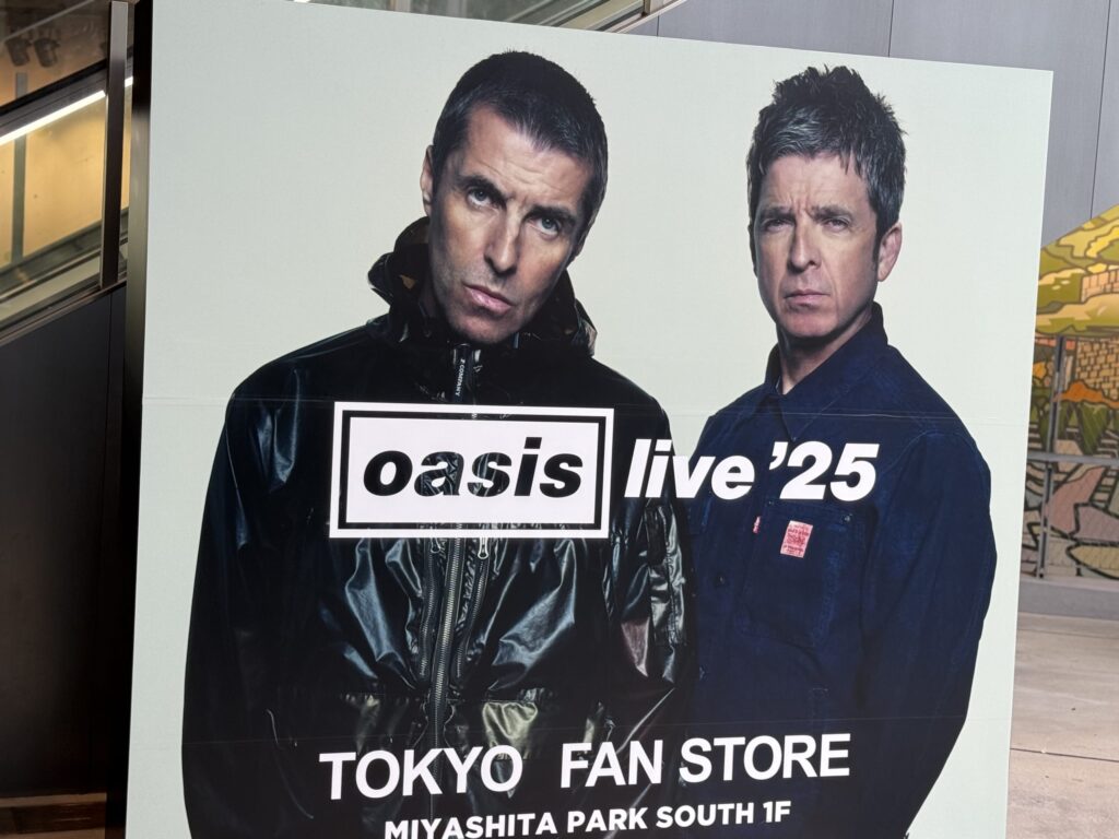 オアシスのリアム・ギャラガーとノエル・ギャラガーが並んで立っている巨大なポスター。ポスターには「oasis live '25」と「TOKYO FAN STORE MIYASHITA PARK SOUTH 1F」の文字が書かれている。