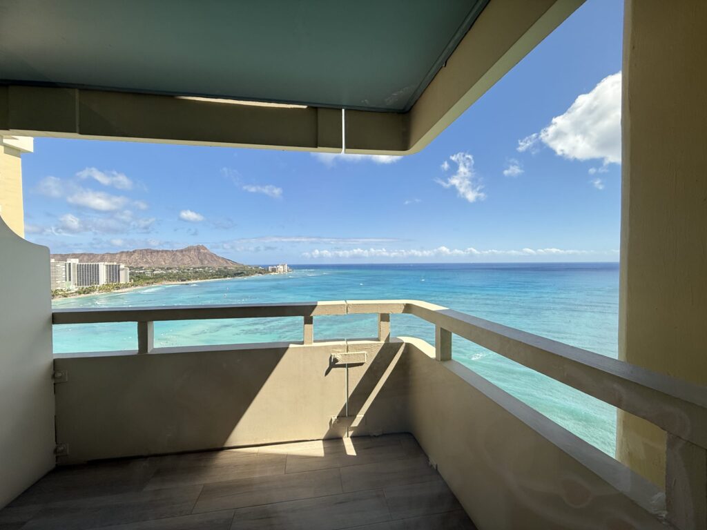 A view of the blue ocean, sky, and Diamond Head in the distance, seen from a high-rise balcony.