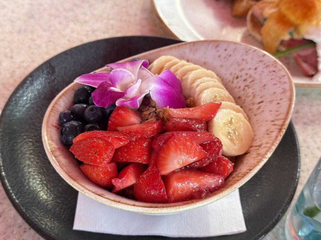A close-up shot of an açaí bowl topped with plenty of strawberries, blueberries, and bananas, garnished with a purple flower.