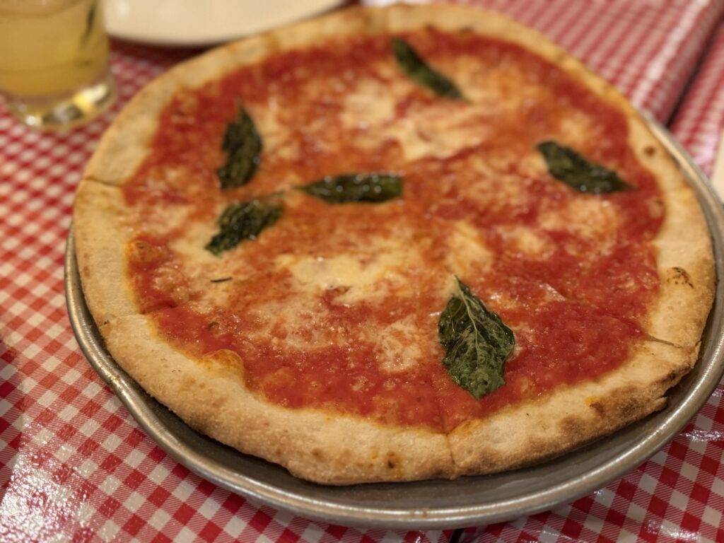 A freshly baked Margherita pizza on a metal tray, placed on a red and white checkered tablecloth.