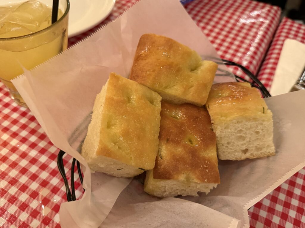 Focaccia bread cut into squares and glistening with olive oil, served in a wire basket on a red and white checkered tablecloth.