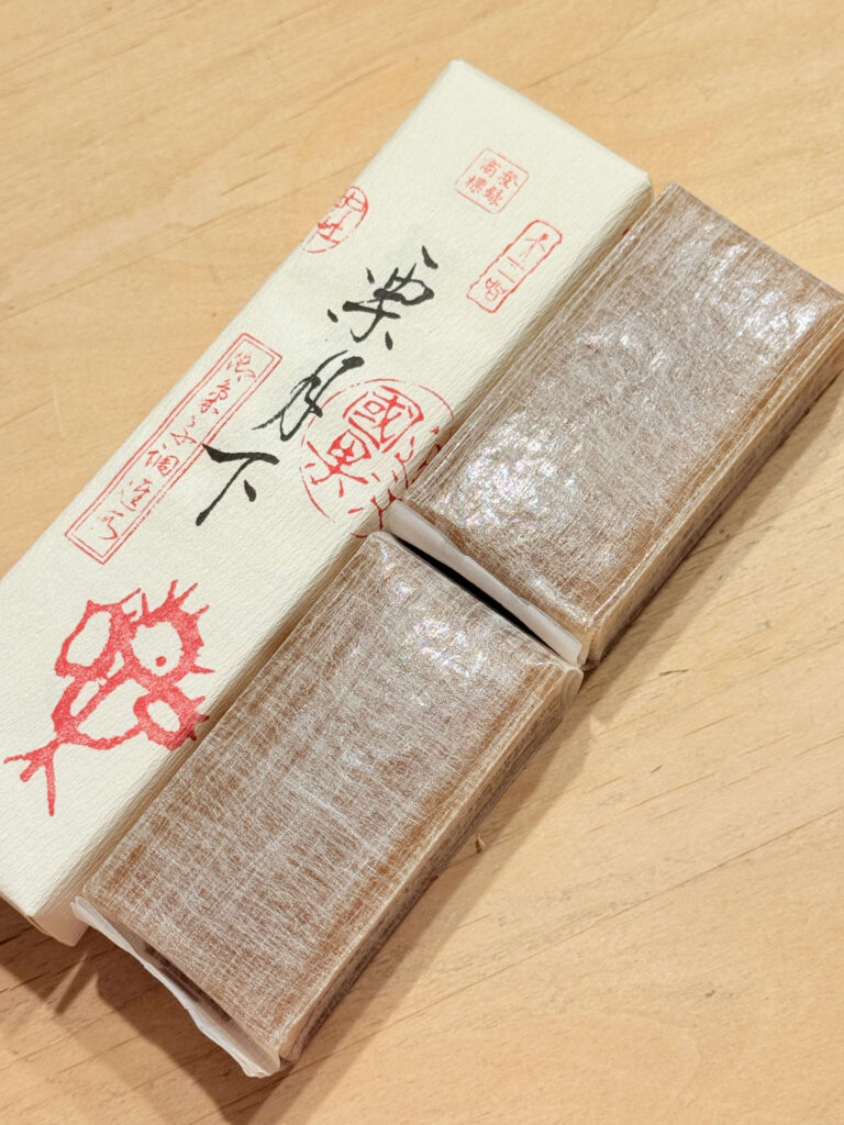 木製のテーブルの上に置かれた、白い箱と中身の栗むし羊羹。羊羹は2つに分かれており、薄紙に包まれている。