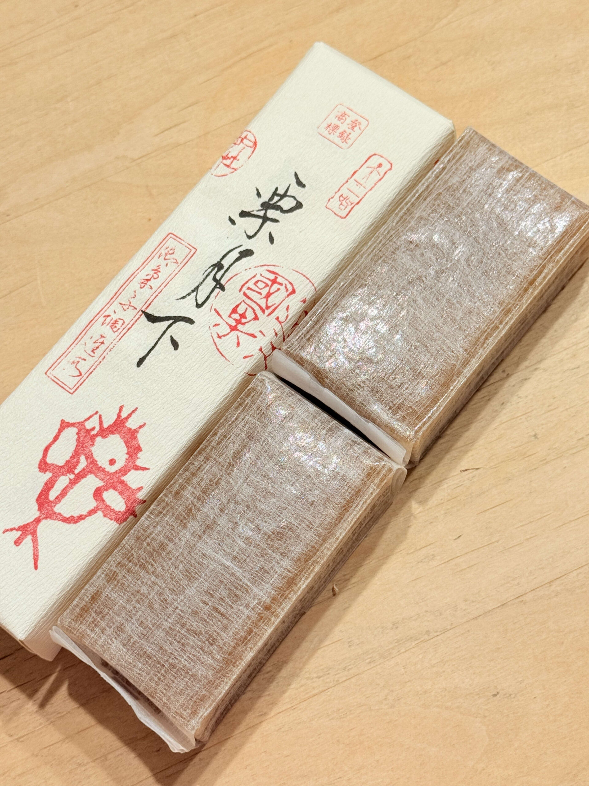 木製のテーブルの上に置かれた、白い箱と中身の栗むし羊羹。羊羹は2つに分かれており、薄紙に包まれている。