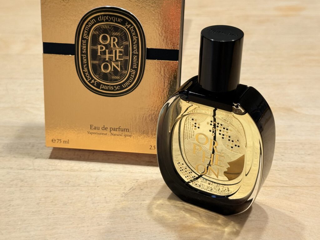 木製のテーブルの上に置かれた、diptyque(ディプティック)の香水「オルフェオン」の限定デザインボトルと金色の箱。