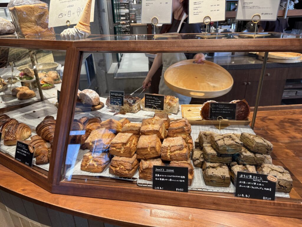 A wooden bakery display case filled with pastries like croissants, bank's scones, and hojicha scones.