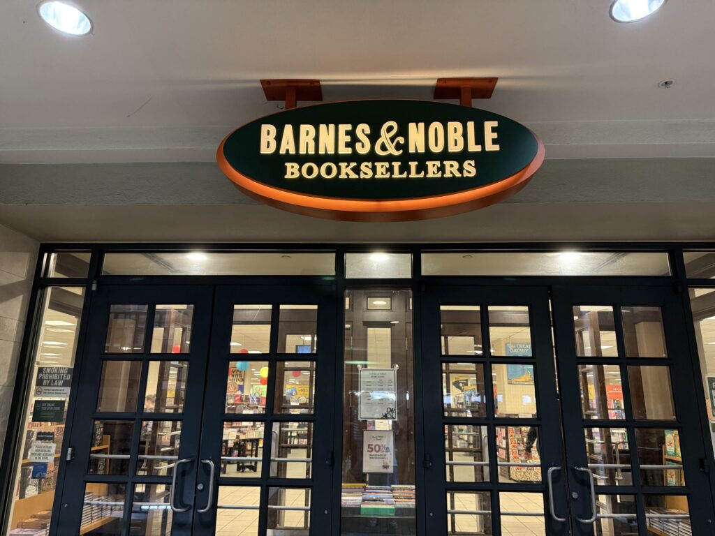 The front entrance of a Barnes & Noble bookstore, featuring its iconic illuminated green and orange oval sign.