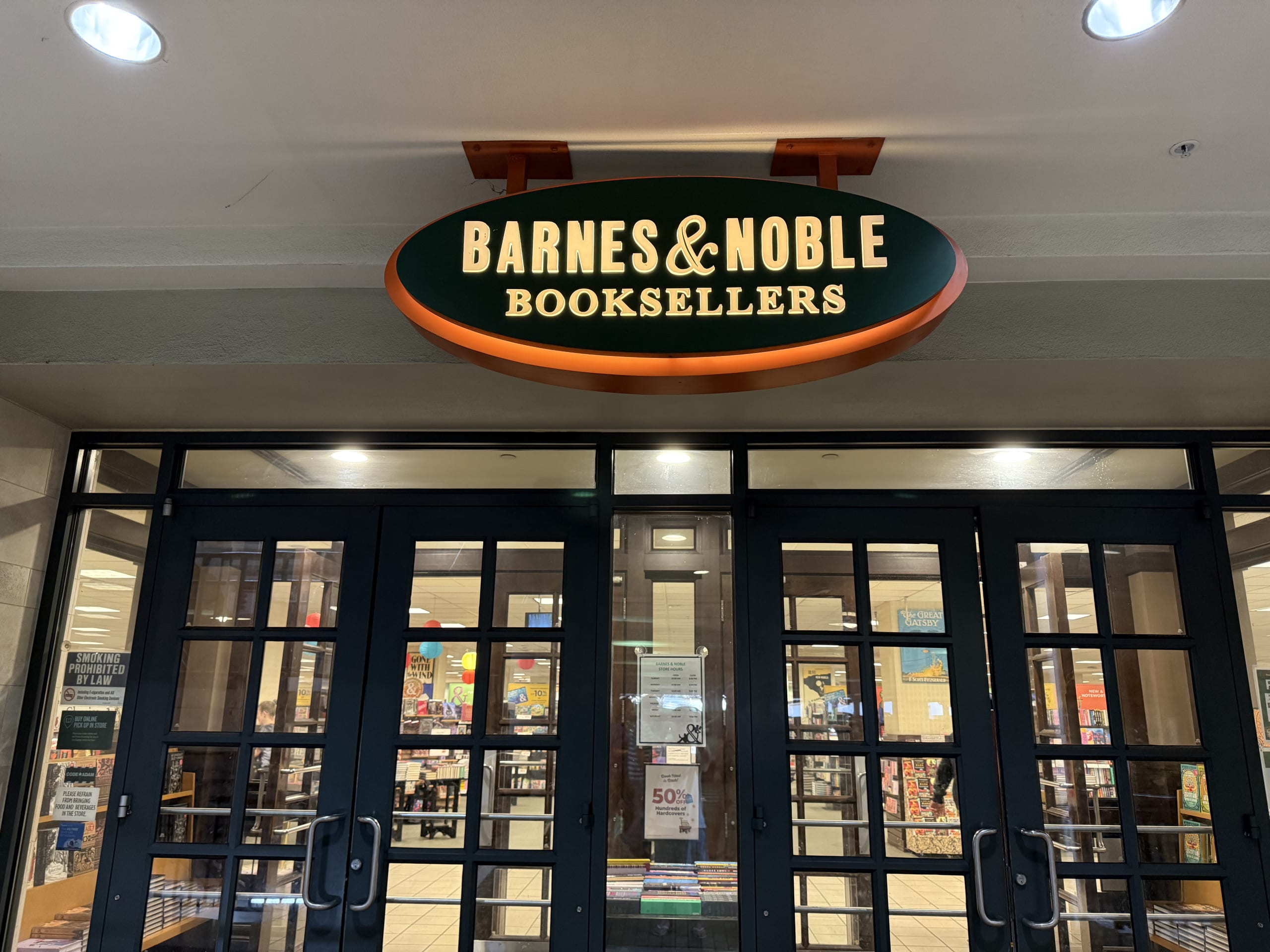 The front entrance of a Barnes & Noble bookstore, featuring its iconic illuminated green and orange oval sign.