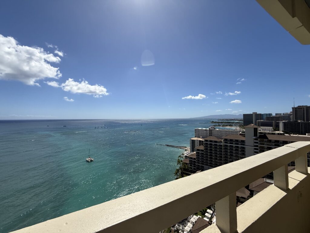 A view of the Waikiki sea and coastline from a hotel balcony on a sunny day.