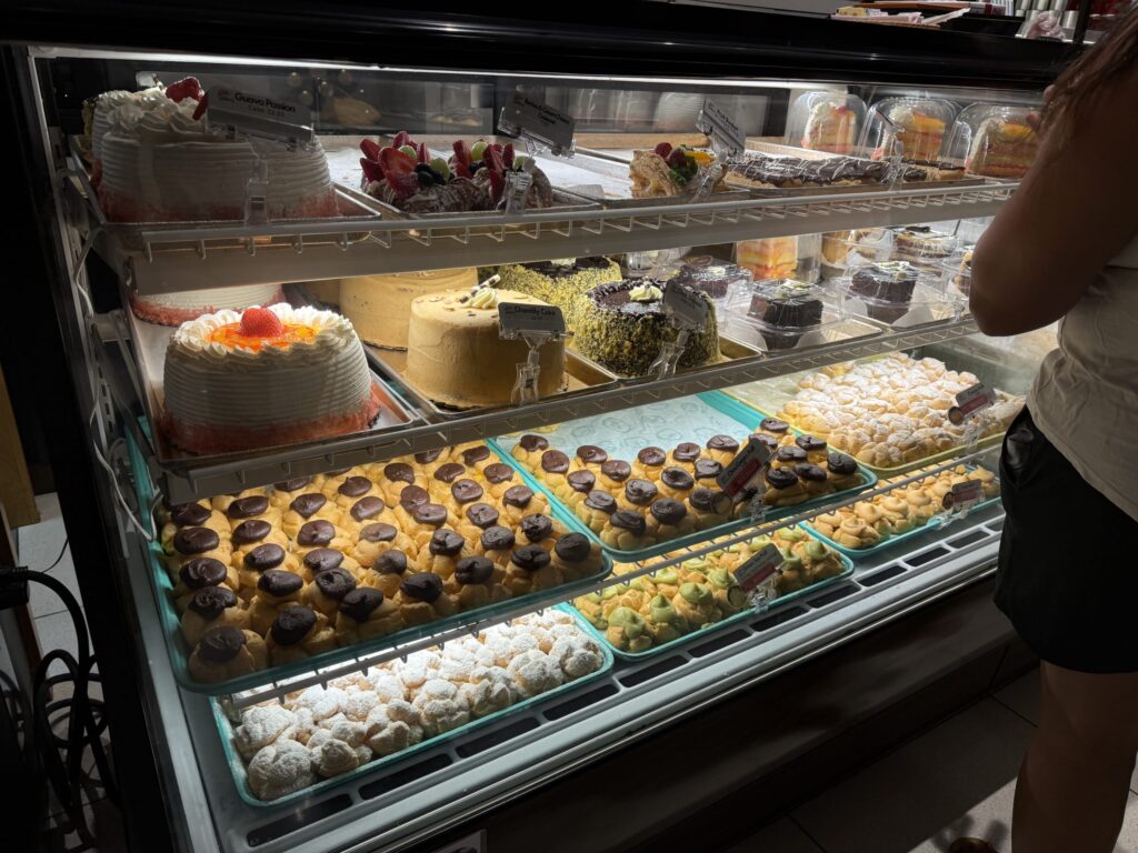 A refrigerated display case at a bakery filled with a wide variety of pastries, such as cakes and Coco Puffs (cream puffs).
