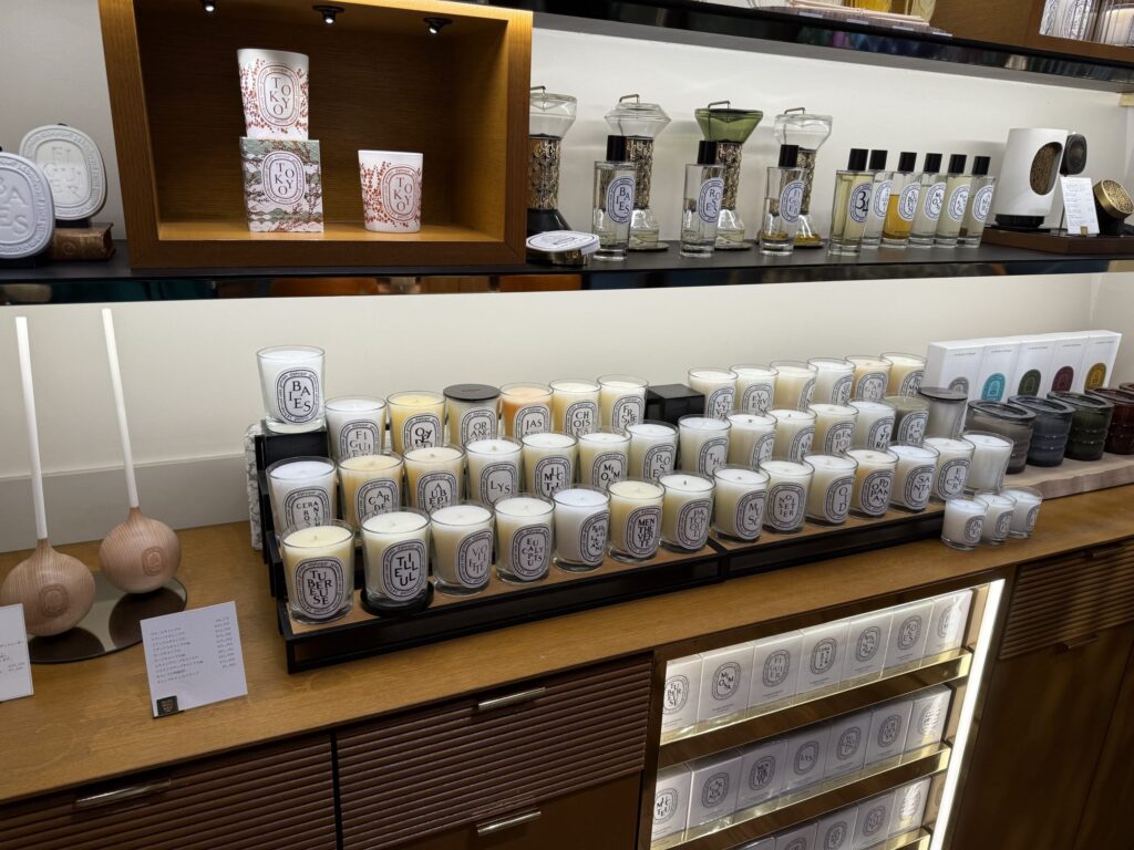 フレグランスブランド、ディプティックの店舗。木製のカウンターと棚に、様々な種類の香りのキャンドルや香水、ディフューザーが美しく陳列されている。