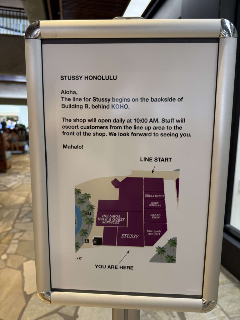 「STUSSY HONOLULU」の店舗案内の看板。入店待ちの列の場所、開店時間、店舗エリアの地図が英語で記載されている。