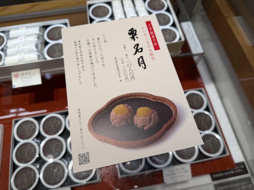 和菓子屋のショーケースに置かれた「栗名月」という和菓子の案内状。カードには栗を乗せたお菓子の写真が印刷されており、背景には商品が並んでいる。