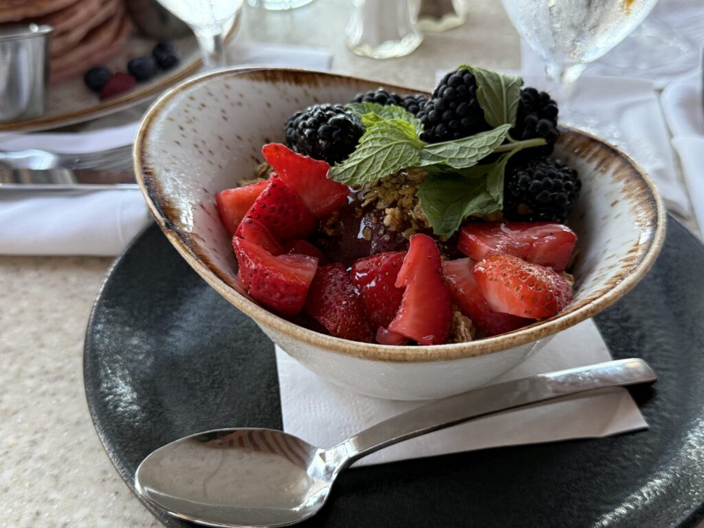 An acai bowl topped with fresh strawberries, blackberries, and mint, served in a rustic white bowl on a black plate.
