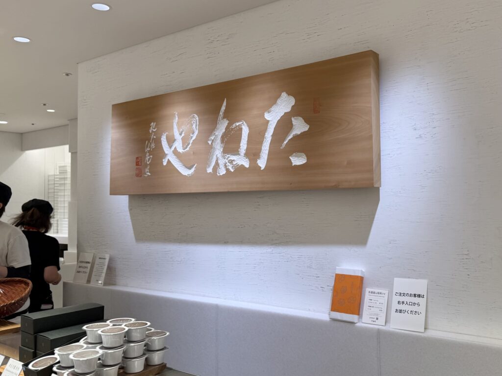 白い壁に掛けられた和菓子店「たねや」の木製看板。白い立体的な筆文字で店名が書かれている。