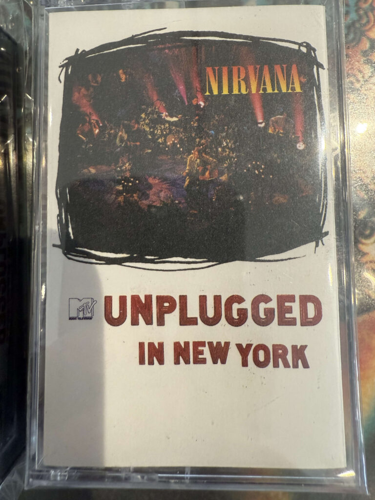 A cassette tape of Nirvana's album 'MTV Unplugged in New York' in its clear plastic case. The cover art shows a photograph of the band performing live on a dimly lit stage.