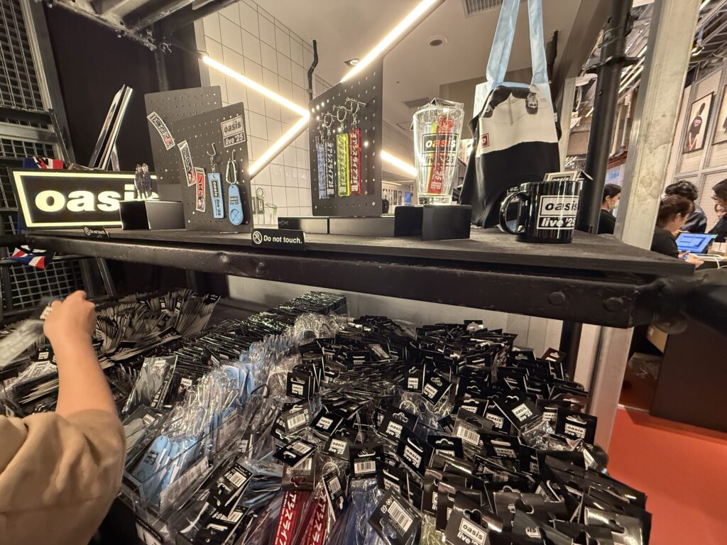 The Oasis live merchandise stand. Keychains, mugs, and tote bags with the