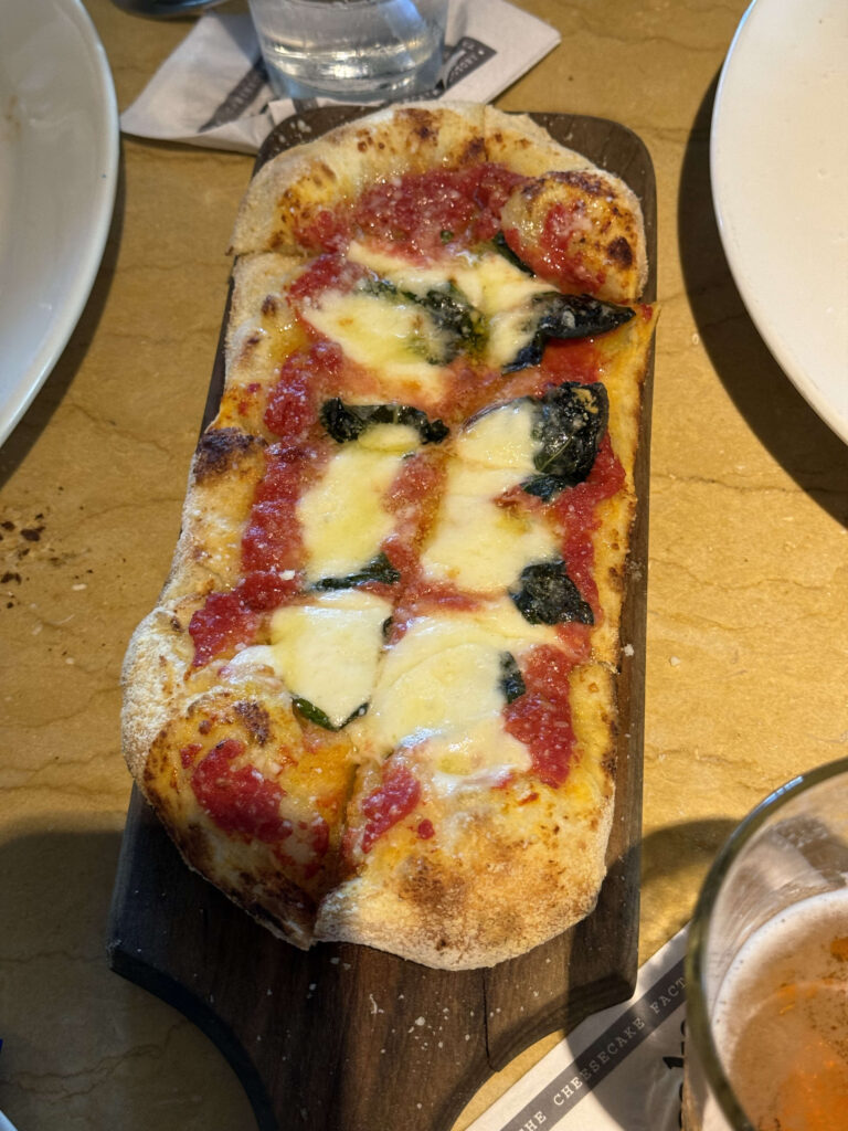 A rectangular Margherita pizza on a wooden board, placed on a restaurant table.