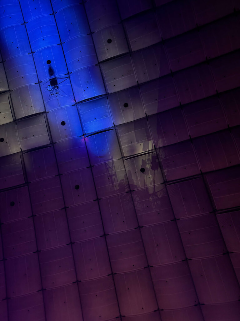 The massive, grid-patterned ceiling of the Tokyo Dome illuminated by a gradient of blue and purple lights.
