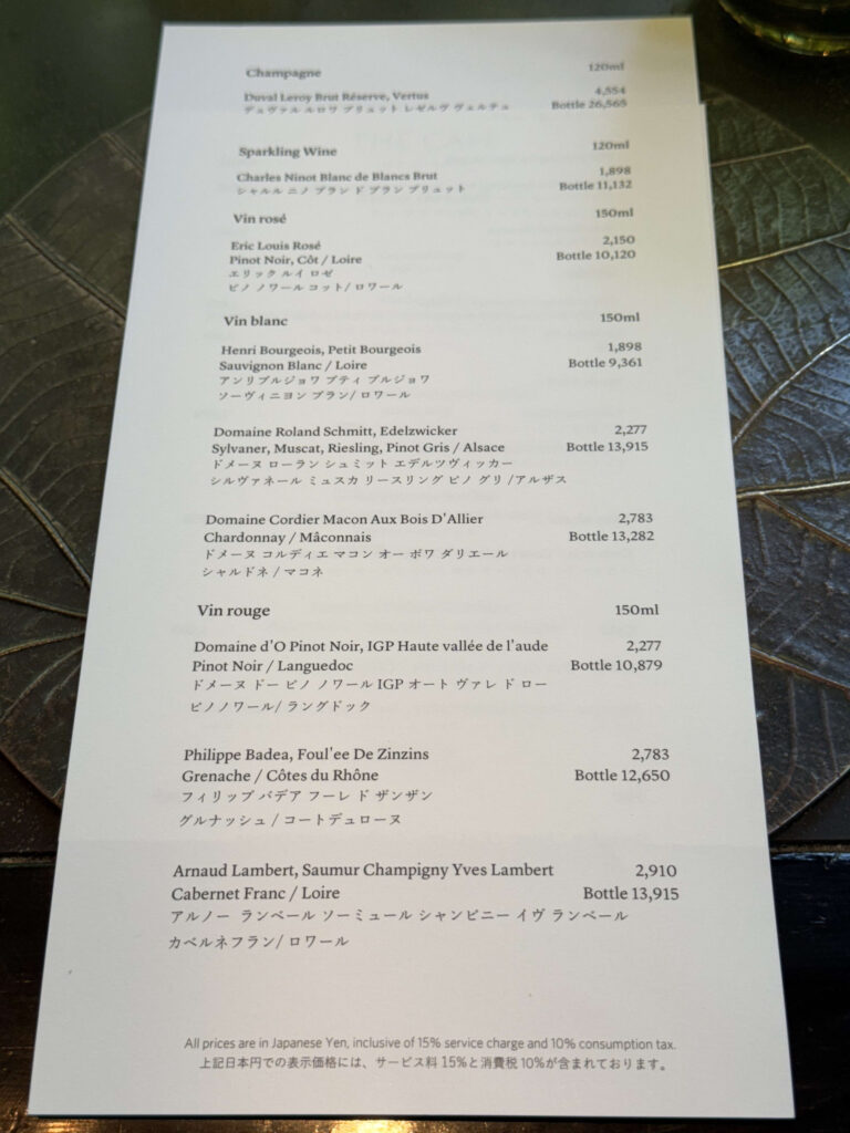 A drink menu listing various champagnes and wines, placed on a dark table with a textured leaf vein pattern.