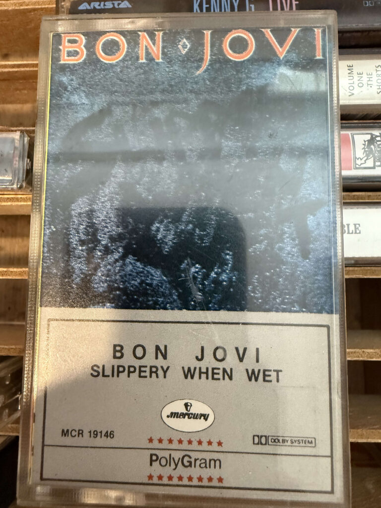 A close-up of the Mexican version of Bon Jovi's 'Slippery When Wet' album on a cassette tape, sitting on a wooden shelf.