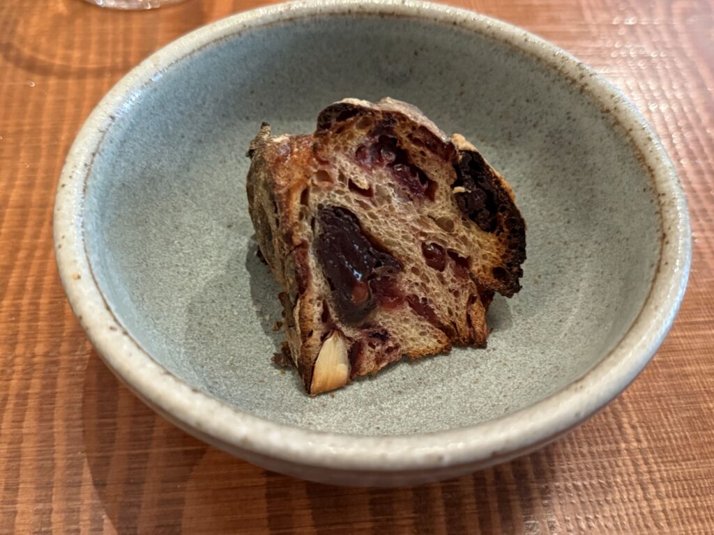 A slice of cacao almond chocolate bread in a rustic ceramic bowl on a wooden table.