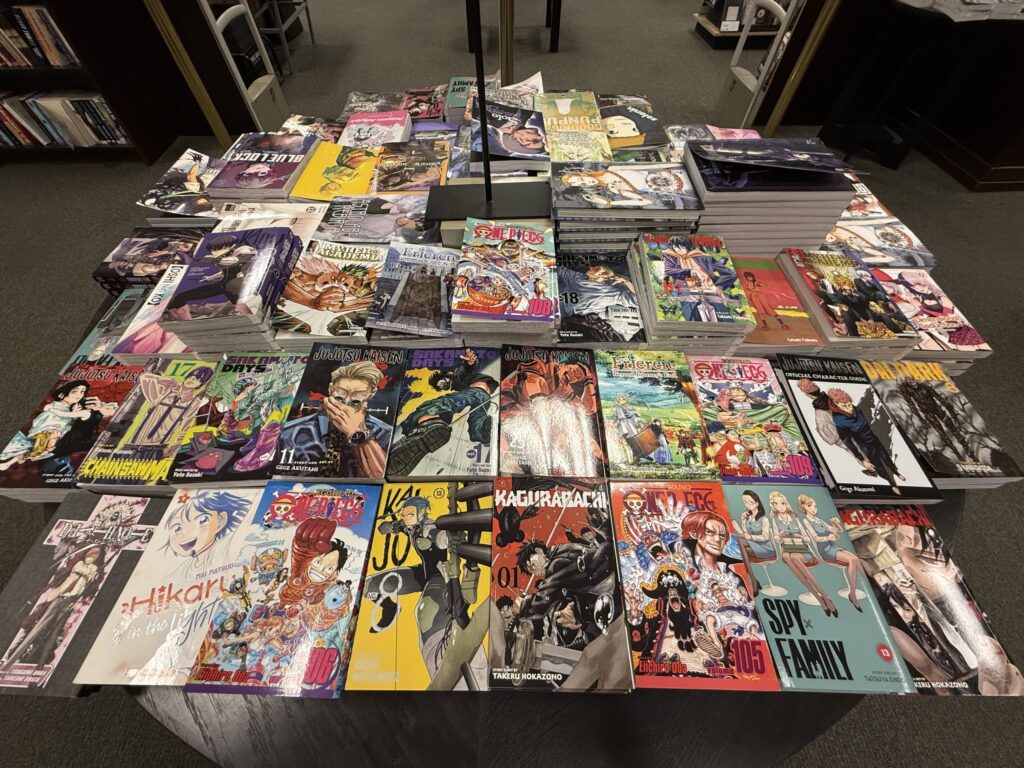 書店のテーブルに山積みされた、様々な種類の日本の漫画の英語版。『呪術廻戦』、『SPY×FAMILY』、『ONE PIECE』など人気作品の表紙が見える。