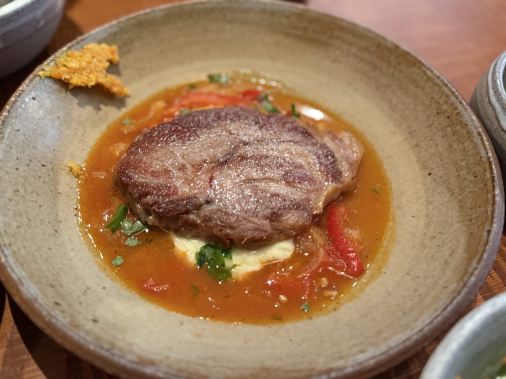 Pork confit in an orange sauce, served in a rustic ceramic bowl with a side of orange confiture on the rim.