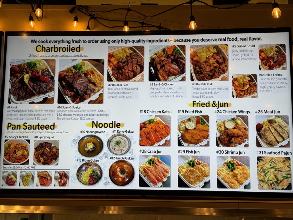 韓国料理レストランの電光メニューボード。カルビ、BBQチキン、麺類、揚げ物など、様々な料理の写真と説明がカテゴリー別に表示されている。