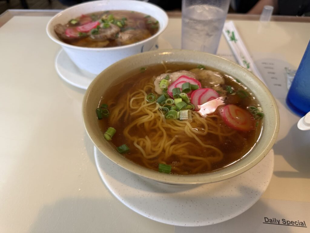 Two bowls of ramen on a table, topped with chashu pork, narutomaki fish cakes, and green onions.