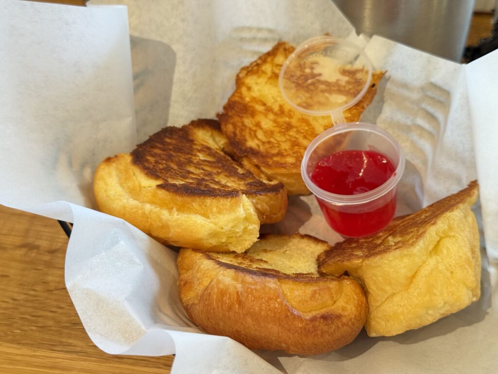 Grilled butter rolls from Liliha Bakery served in a basket, with small cups of red jelly and syrup on the side.