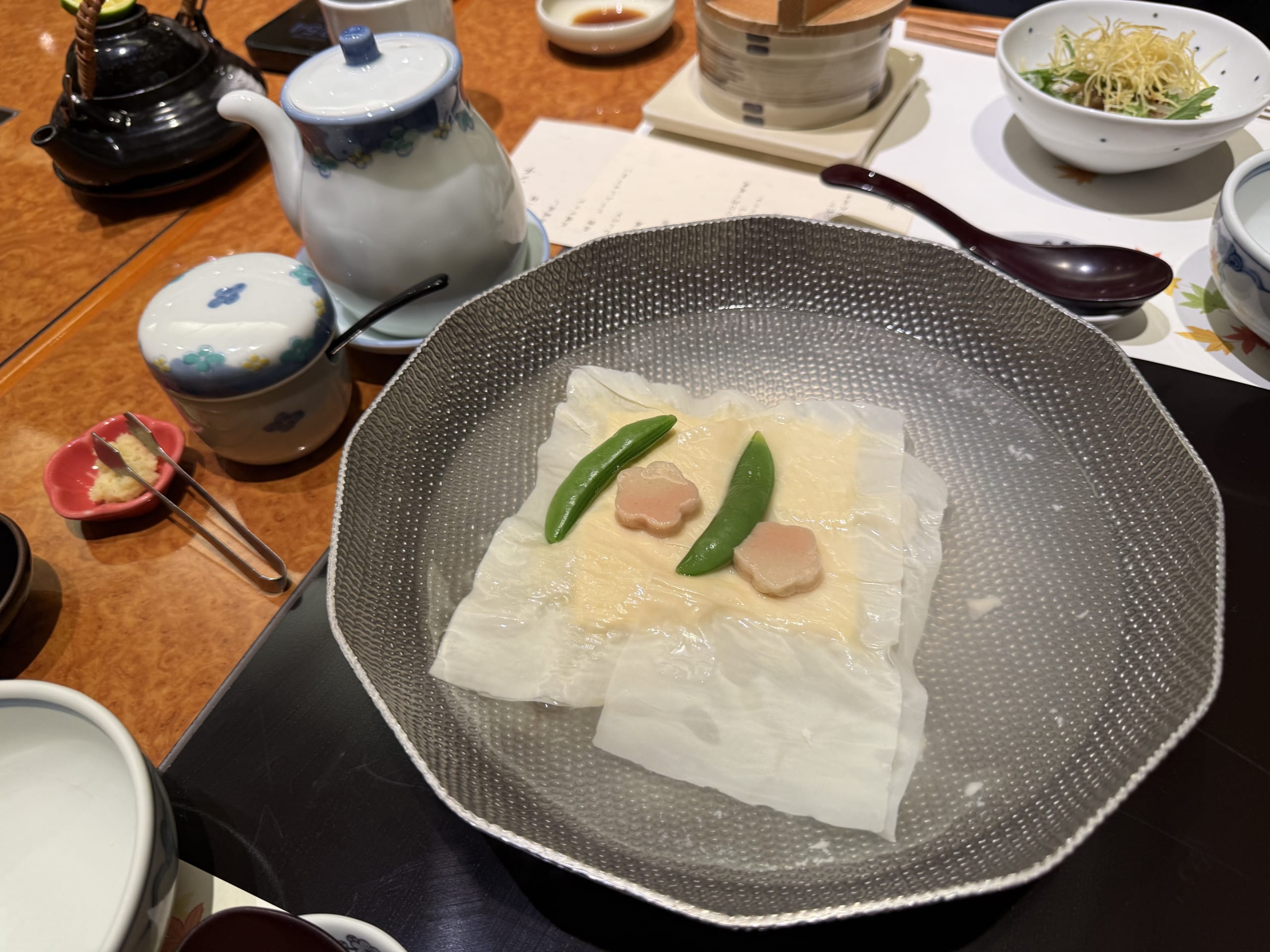 Yudofu, or boiled tofu, served in a hammered metal bowl filled with hot spring water, garnished with snow peas and pink flower-shaped fu.