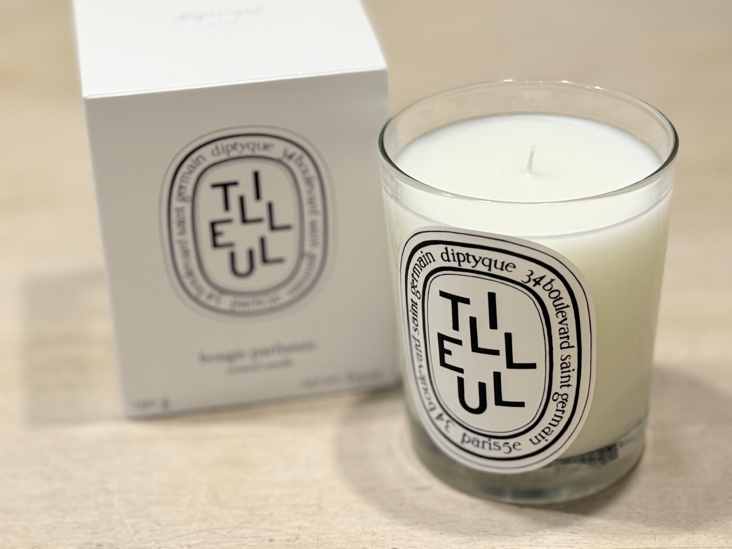 明るい木製のテーブルの上に置かれた、diptyque（ディプティック）のキャンドル「Tilleul（ティユル）」と白いパッケージボックス。