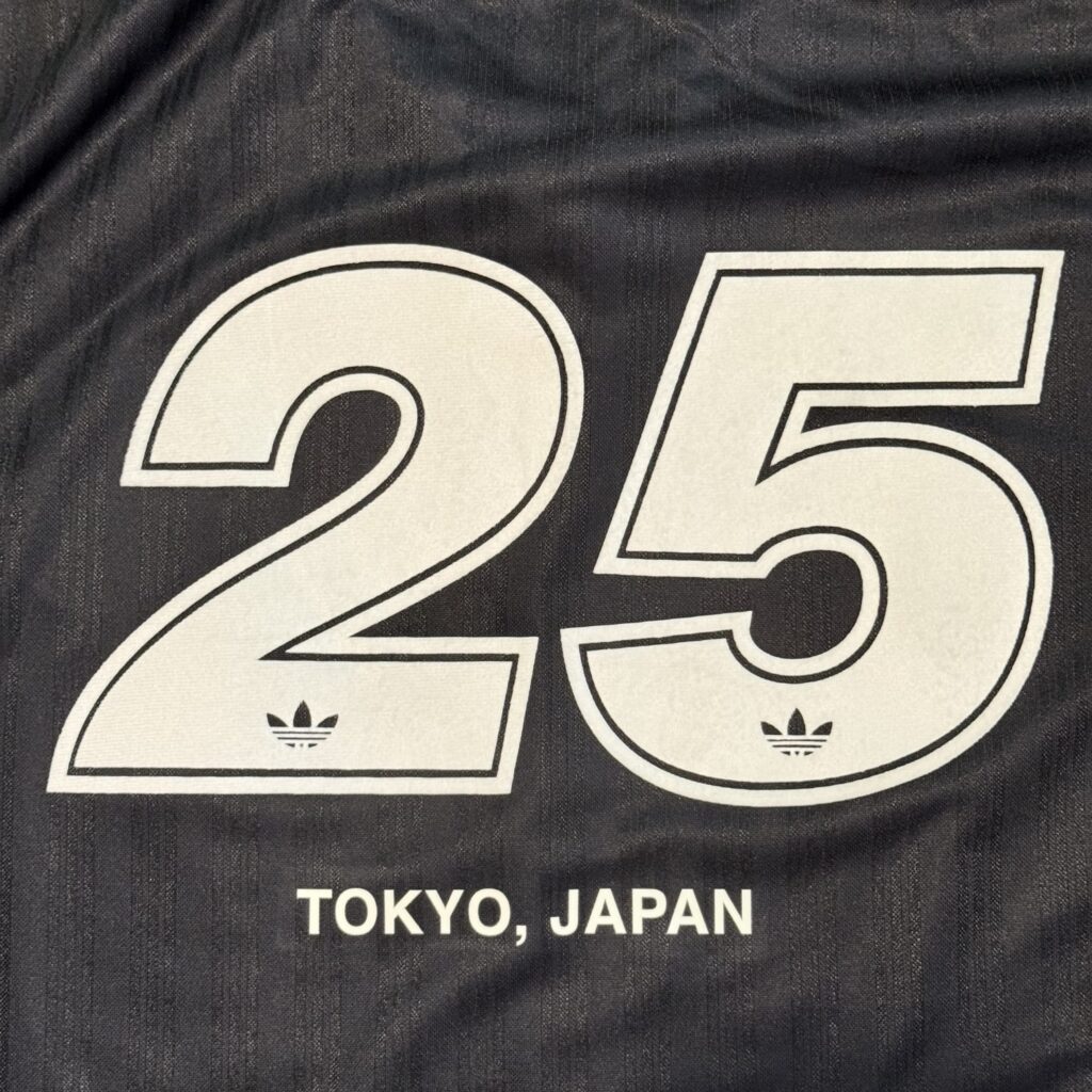 A close-up of the back of a black jersey, featuring the number '25' in white with an Adidas Trefoil logo inside, and the text 'TOKYO, JAPAN' printed below.