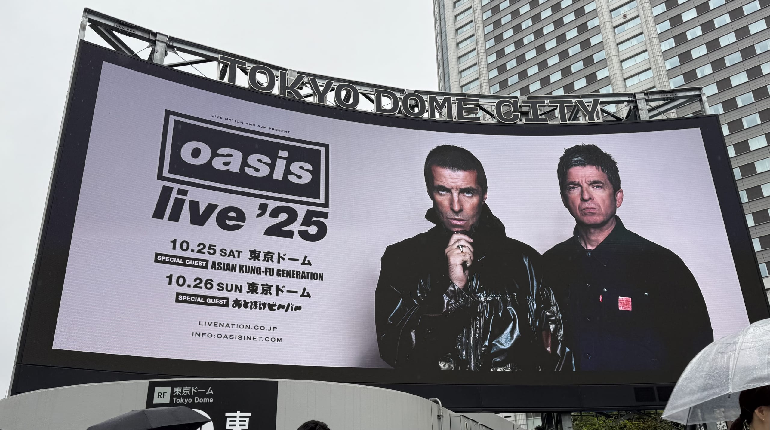 東京ドームシティの大型スクリーンに映し出された、オアシス(Oasis)の来日公演「live '25」の告知。リアム・ギャラガーとノエル・ギャラガーの写真と共に、東京ドームでの公演日程とスペシャルゲストが記載されている。