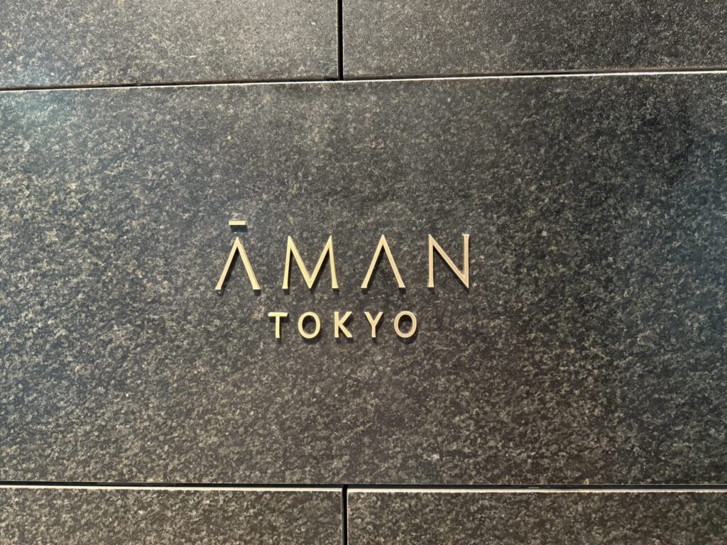 The gold logo for 'AMAN TOKYO' mounted on a dark granite stone wall.