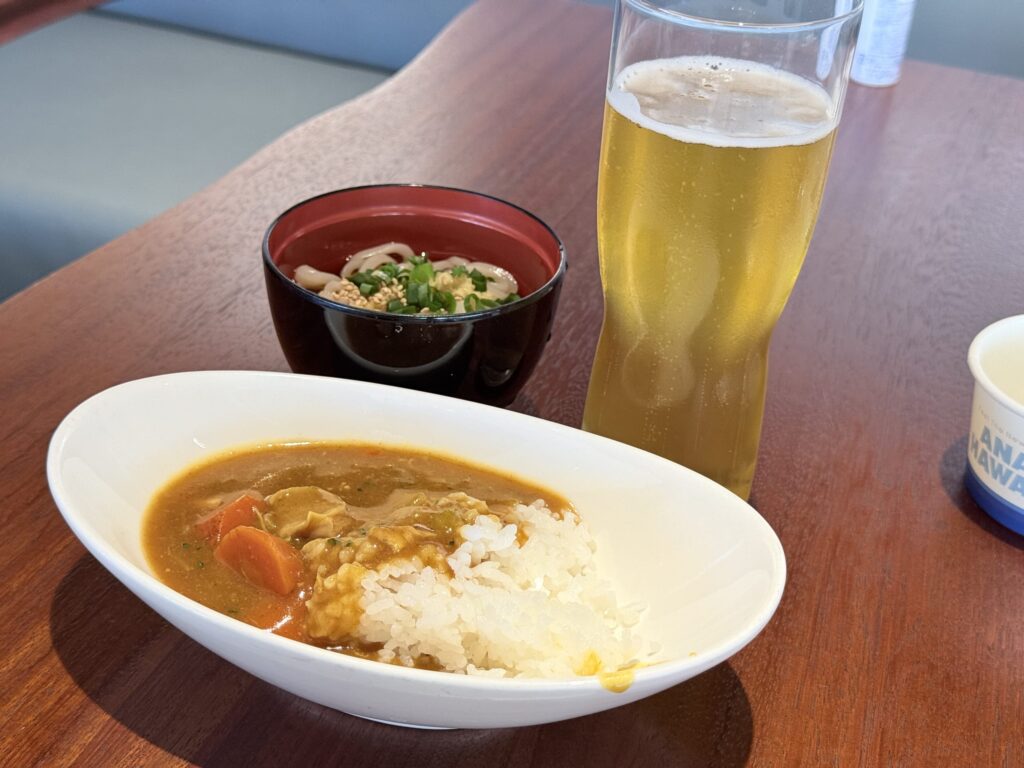 A set of Japanese curry rice, cold udon noodles, and a glass of beer arranged on a wooden table.