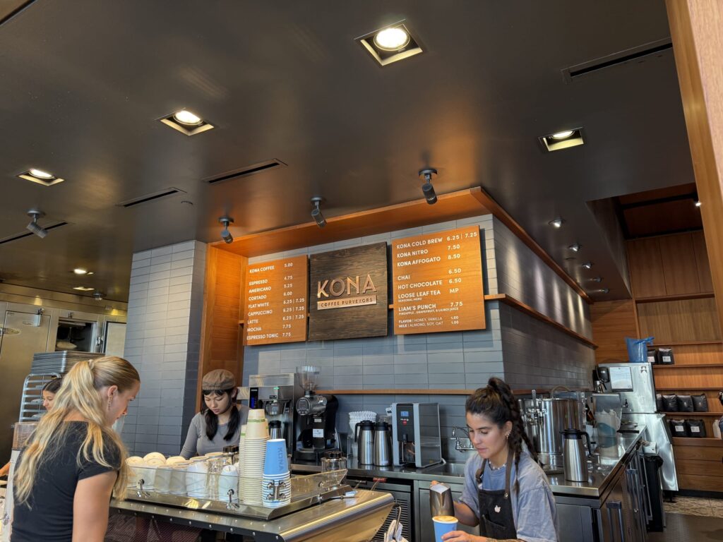 The interior counter of Kona Coffee Purveyors. A barista is preparing coffee, and a wooden menu board hangs on the wall.