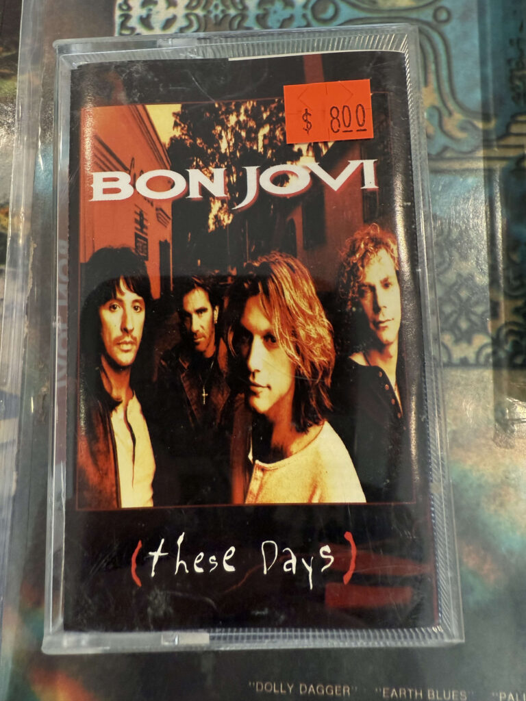 A cassette tape of the Bon Jovi album 'These Days' in a plastic case. An orange price tag showing $800 is stuck to the front.