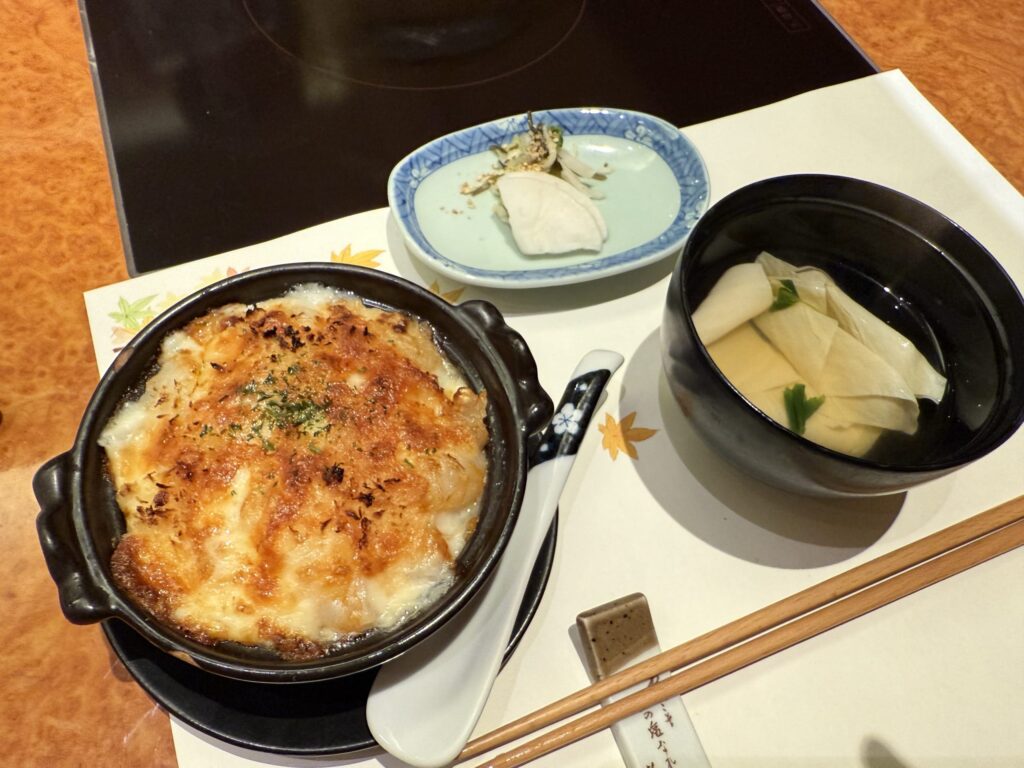 A Japanese meal set on a table, featuring a shrimp doria, a bowl of yuba soup, and a side of pickles.