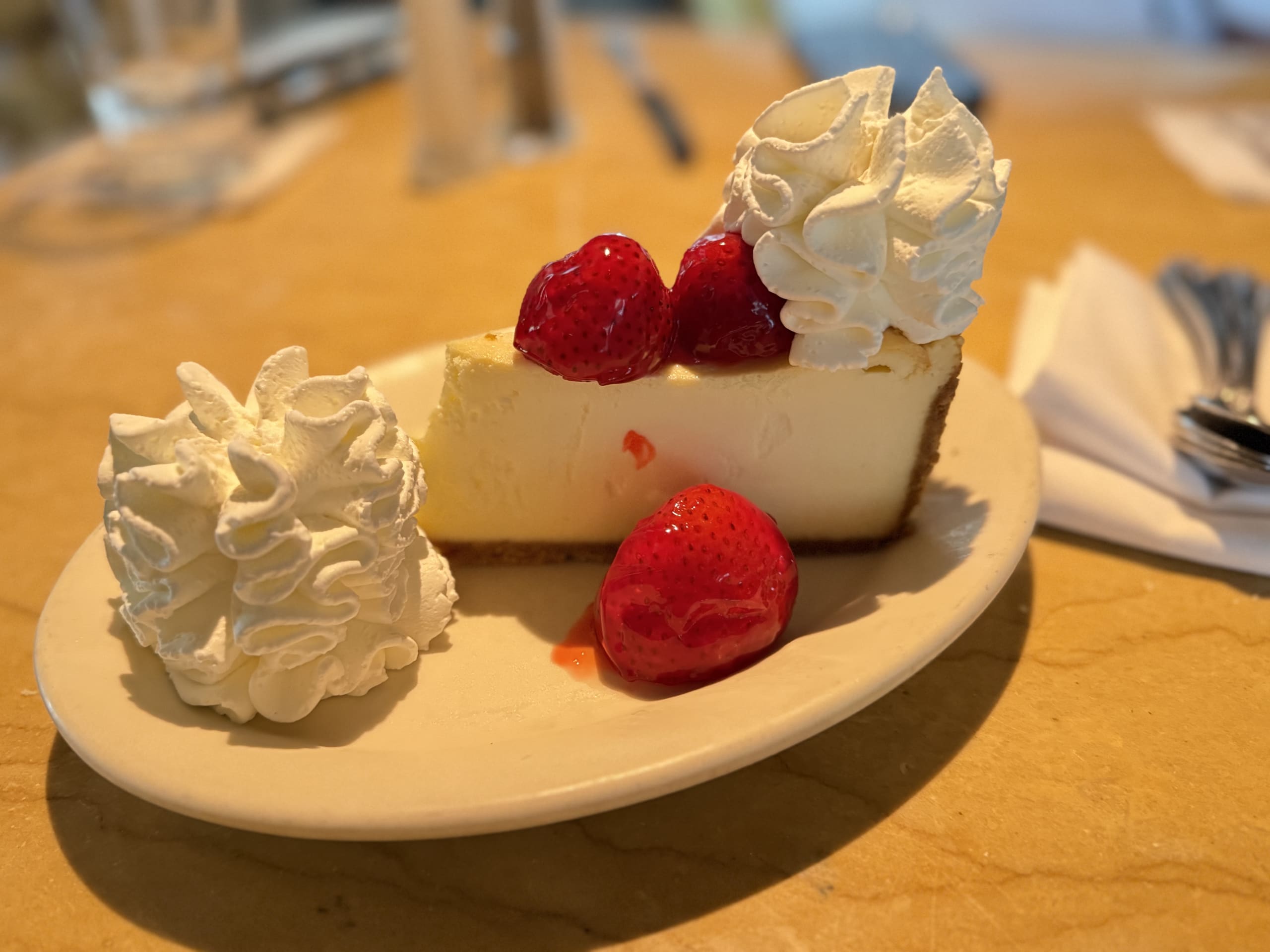 A slice of strawberry cheesecake topped with whipped cream, served on a white plate on a wooden table.