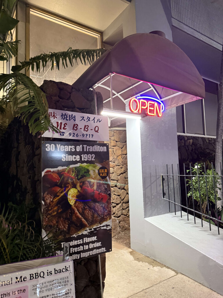 夜のME B-B-Qレストランの入り口。赤いネオンのOPENサインと、カルビプレートの写真が載った看板が立っている。