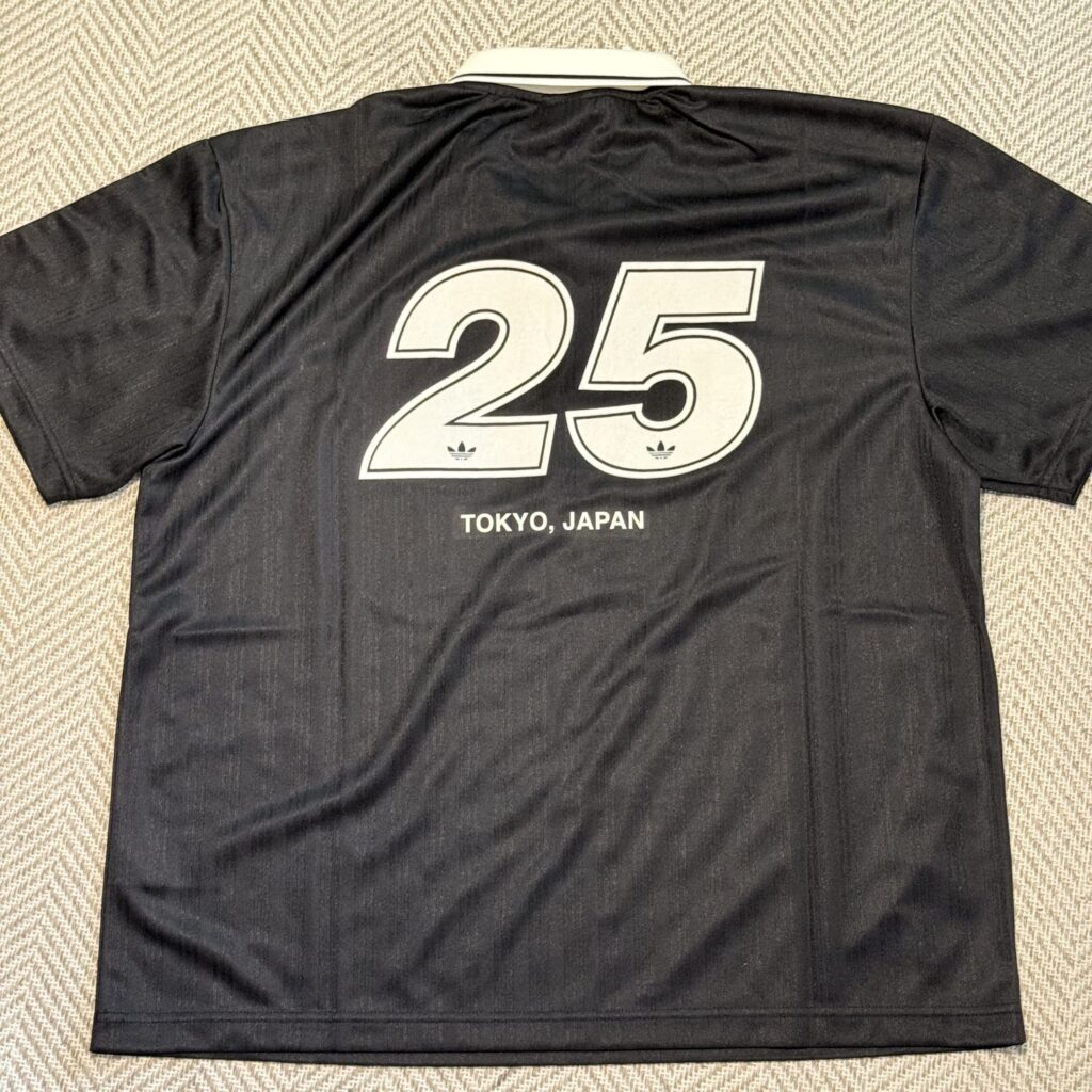 The back of a black Adidas game shirt spread out on a herringbone-patterned floor. The number '25' is printed largely in white, with the words 'TOKYO, JAPAN' and the Adidas logo visible below it.