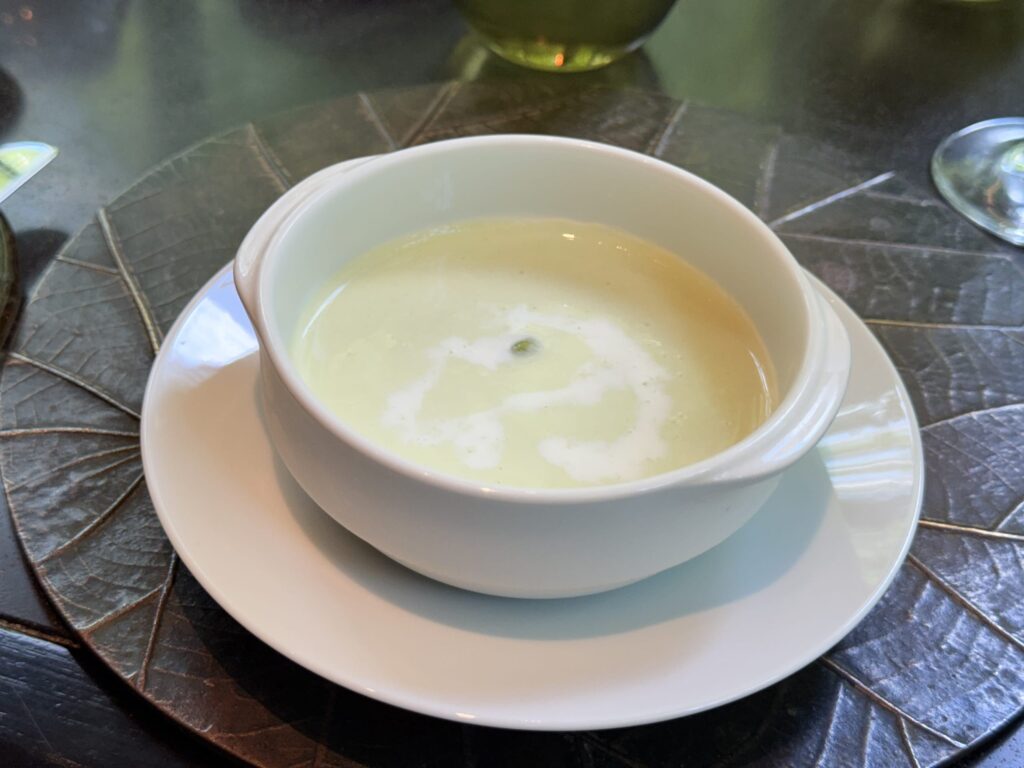 A white bowl of cream-colored seasonal soup, placed on a dark, leaf-shaped placemat.