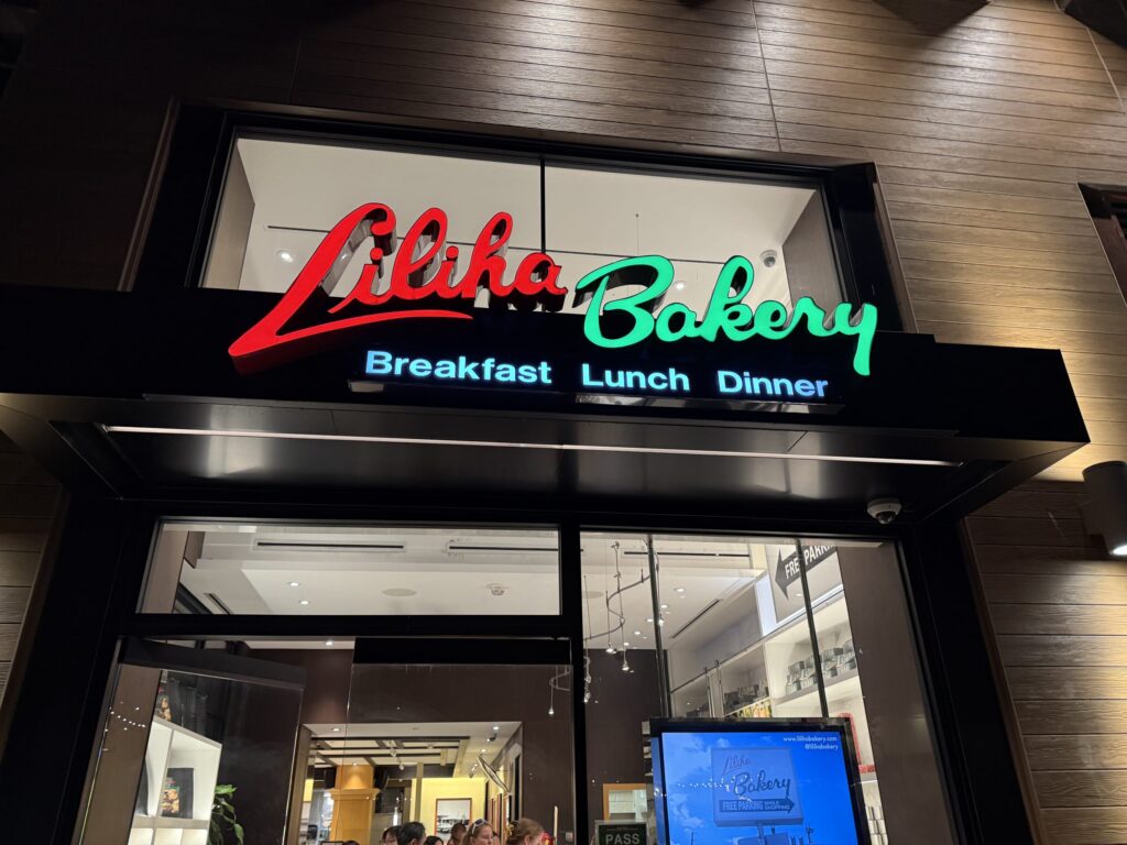 夜のインターナショナルマーケットプレイスにあるリリハベーカリーの店舗外観。赤色の「Liliha」と緑色の「Bakery」という文字のネオンサインが輝いている。