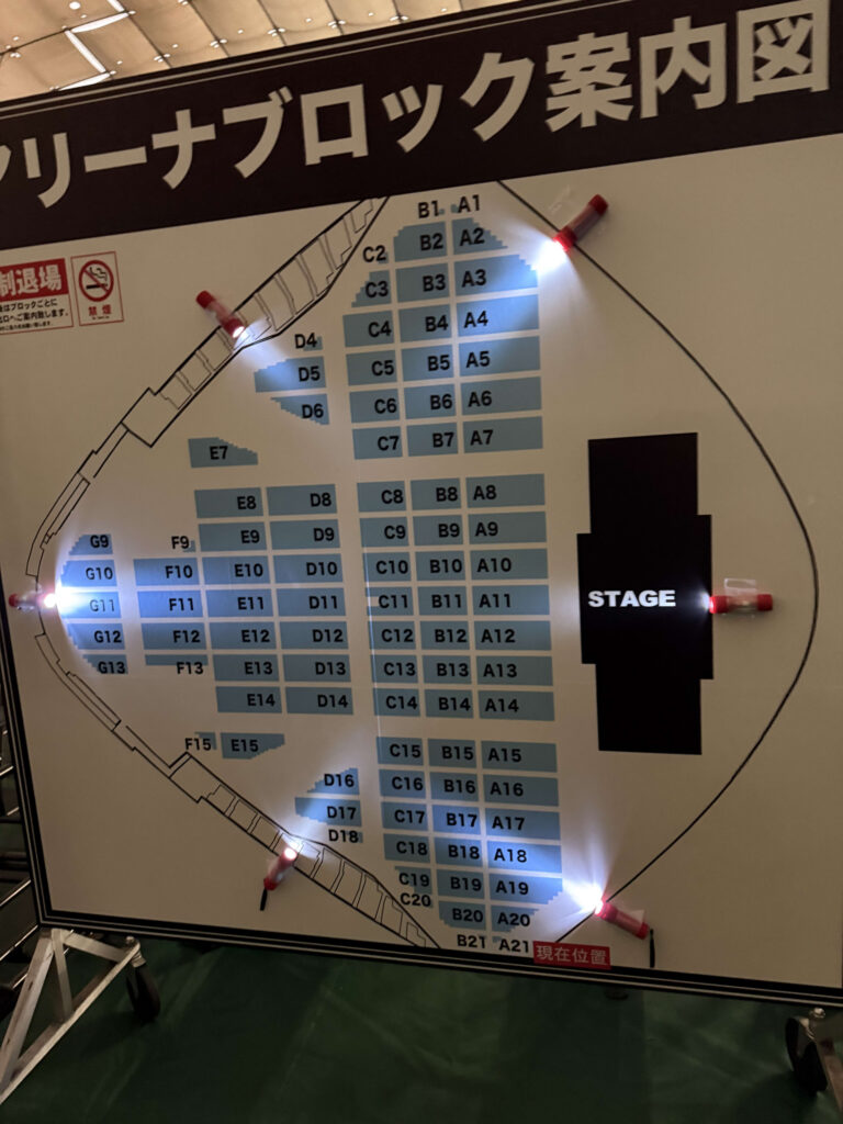 コンサート会場のアリーナブロック案内図。ステージとAからGまでのアルファベットで分けられた座席ブロックの配置が示されている。右下には「現在位置」という赤い表示がある。