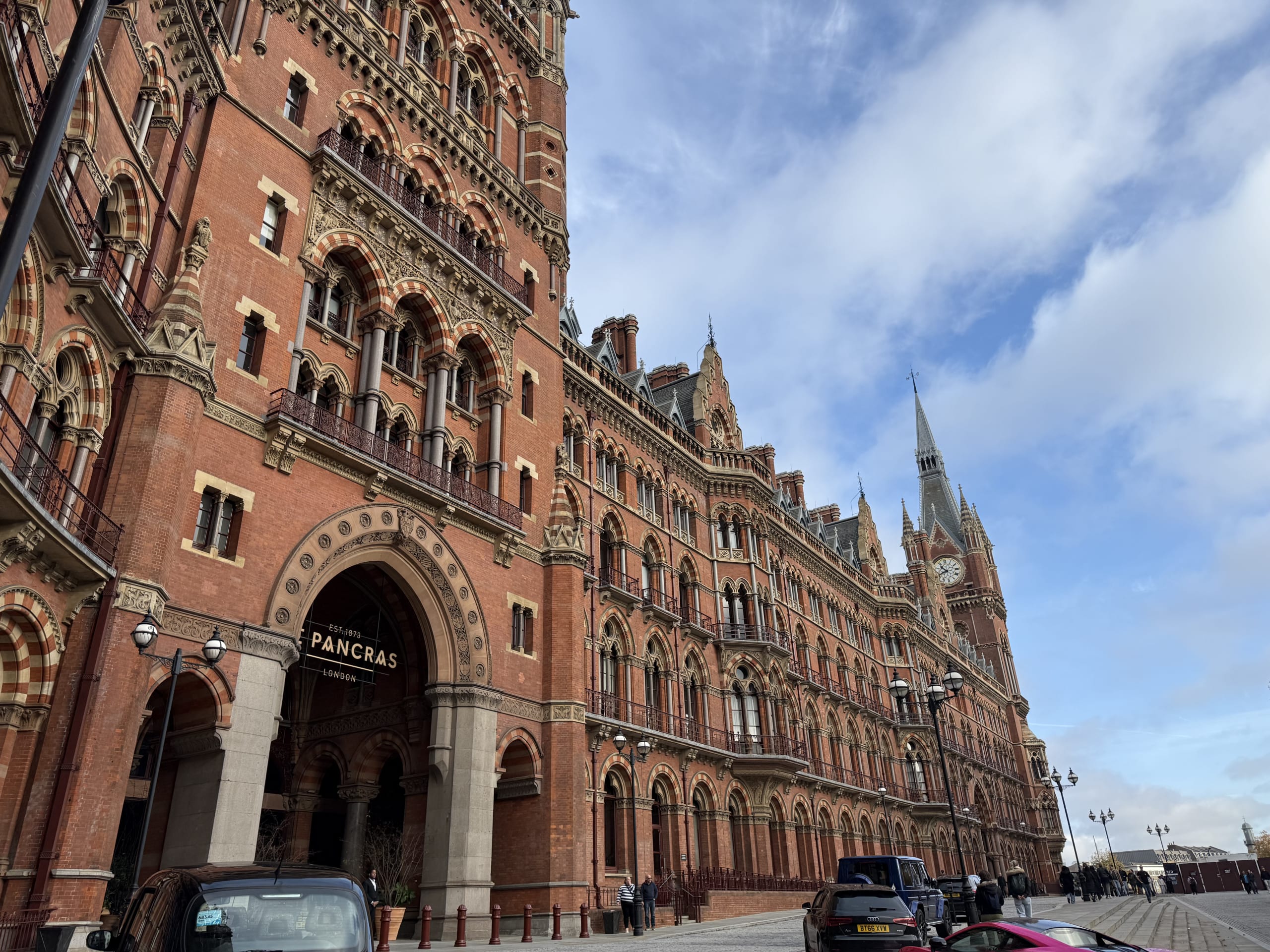 A low-angle shot of the magnificent red-brick Victorian Gothic facade of St Pancras International station in London against a blue sky with clouds.