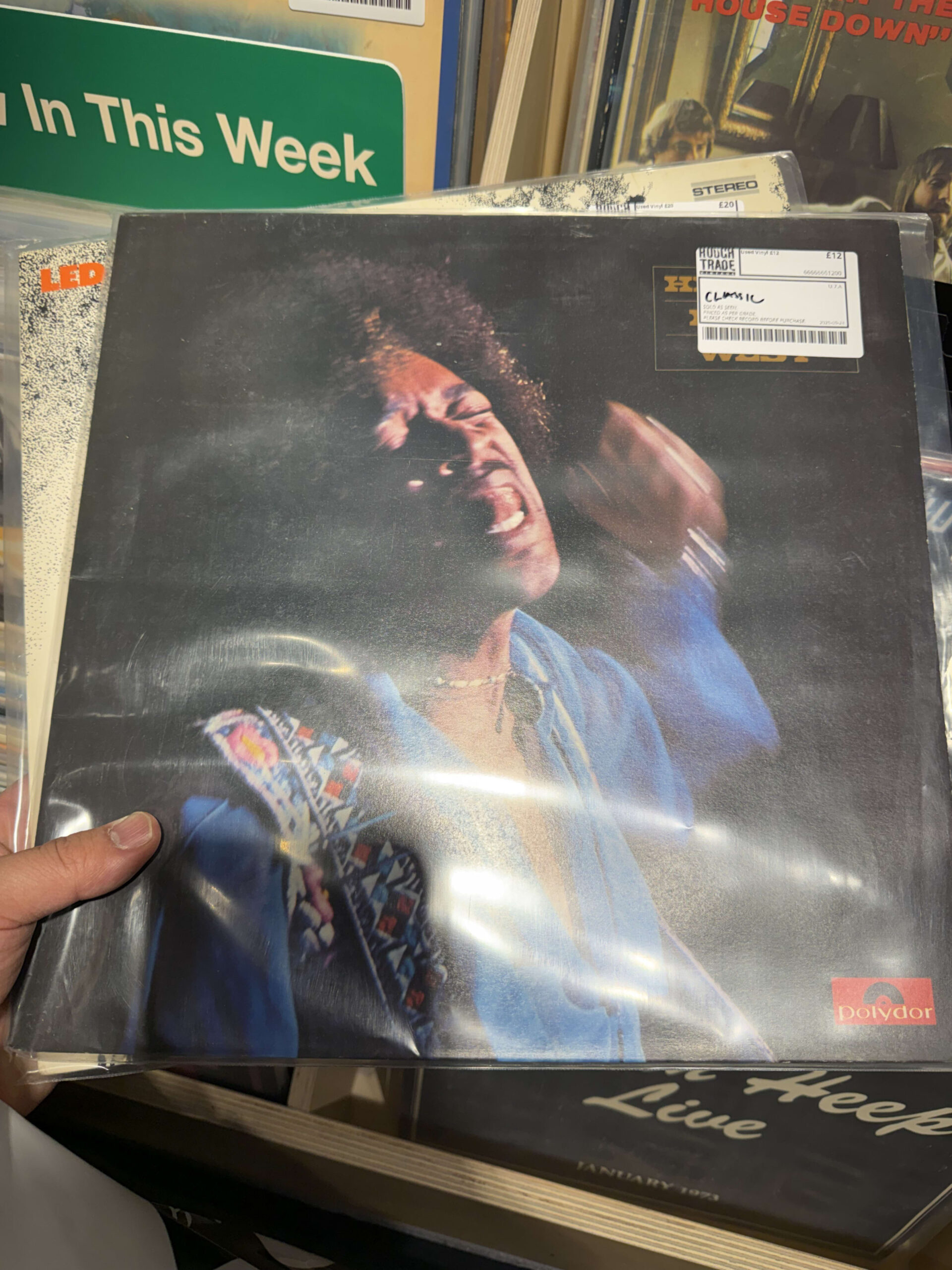 レコード店で手に取られたジミ・ヘンドリックスのアルバム『Hendrix In The West』。ジャケットには、青いジャケットを着て情熱的に歌う彼の姿が写っている。