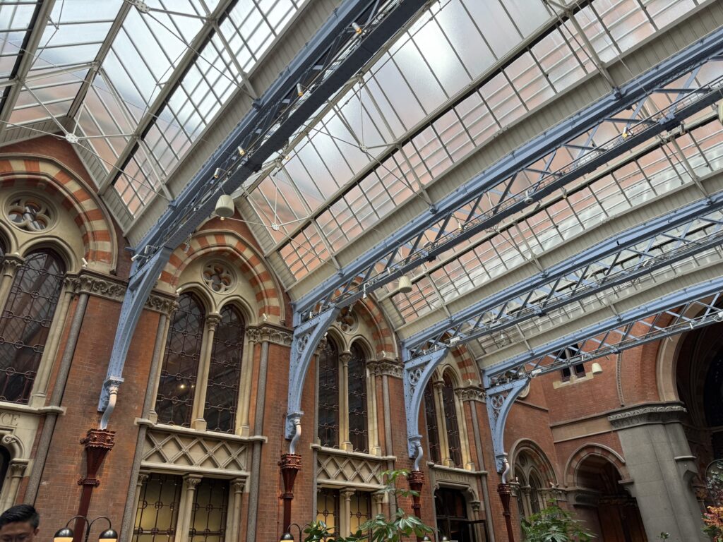 Low angle view of a massive glass roof supported by light blue iron trusses and red brick arches