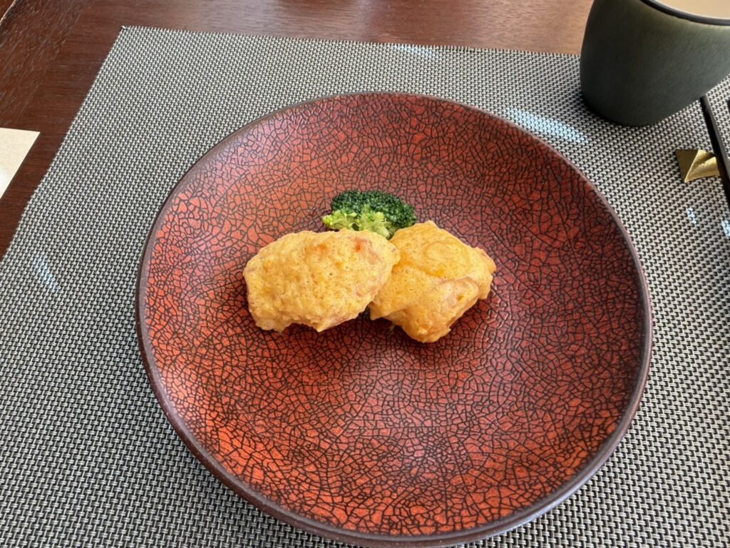 Deep-fried fresh fish with a salted egg sauce, garnished with broccoli and served on a striking red plate with a black crackle pattern.