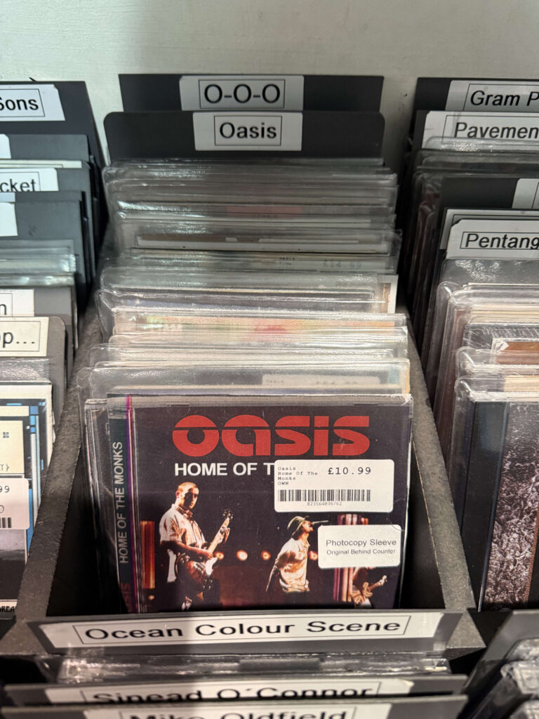 CDs filed alphabetically in a record store rack. A CD by the band Oasis, titled